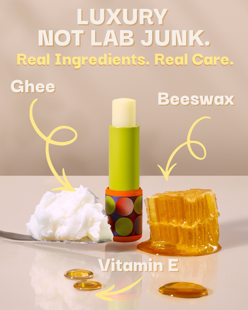 A lip balm stick stands upright in the center on a glossy beige surface, with ingredient callouts and arrows pointing to it: ghee, beeswax, and vitamin E. The balm tube is lime green with a multicolor circular pattern near the base, and the visible balm itself is off-white.